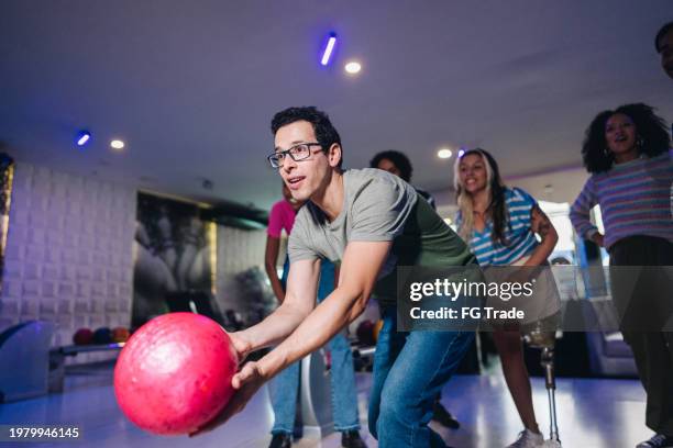 mittlerer erwachsener mann, der mit freunden eine bowlingkugel in einem bowlingclub wirft - bowlingbahn stock-fotos und bilder