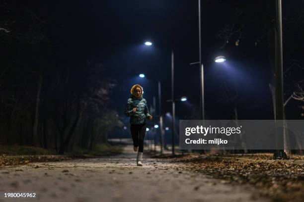 young woman jogging in park at night - donker stockfoto's en -beelden