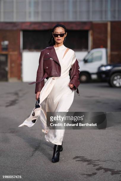 Pornwika Spiecker wears sunglasses, a burgundy leather biker jacket , a white gathered long dress, black leather pointed boots , outside Gestuz,...