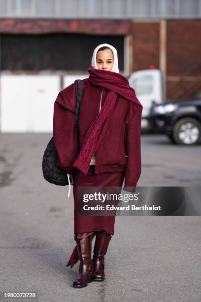 Guest wears a white balaclava, a burgundy full outfit, a long oversized scarf, an oversized jacket with shoulder pads, a midi skirt , leather boots ,...