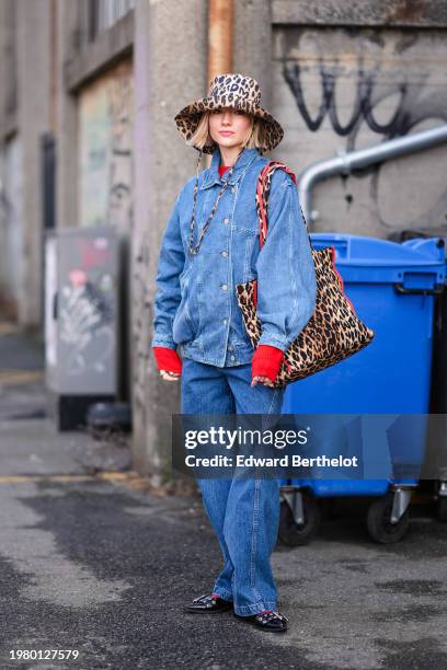 Guest wears a brown leopard print pattern hat, a matching tote bag, a blue denim jacket , blue flared denim jeans pants , a red pullover , pointed...