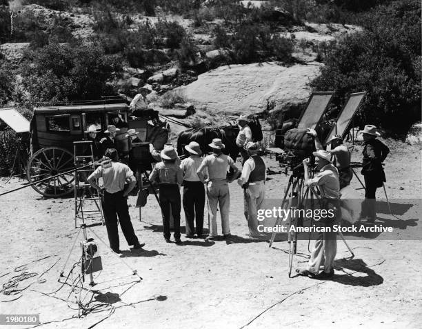 Actor Edward Arnold stands with his costars beside a stagecoach as a film crew prepares to shoot a scene on location for an unidentified Western...