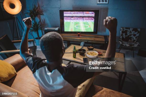 young man watching soccer game at home - championship round one foto e immagini stock