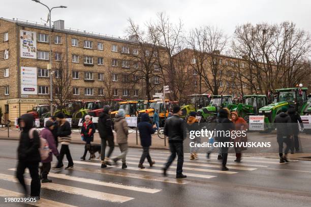 Pedestrians cross a street as farmers with their tractors gather for a demonstration in Jelgava, Latvia on February 5, 2024. Latvian farmers hope to...