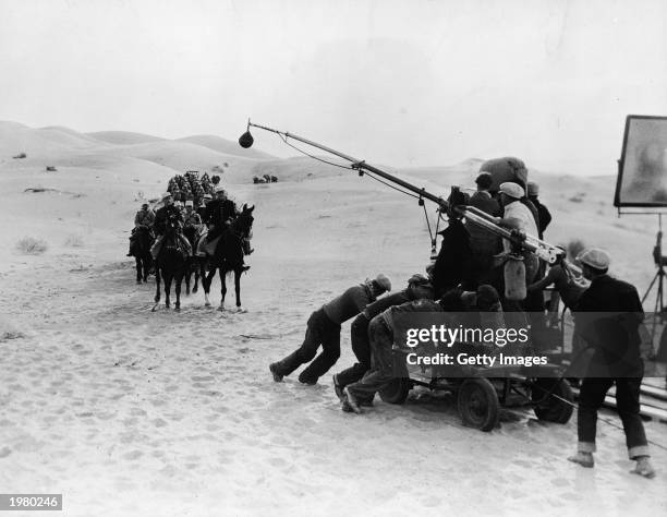 Workers push a dolly platform with a camera crew and a microphone while filming actors Ronald Colman , Victor McLaglen and other French Foreign...