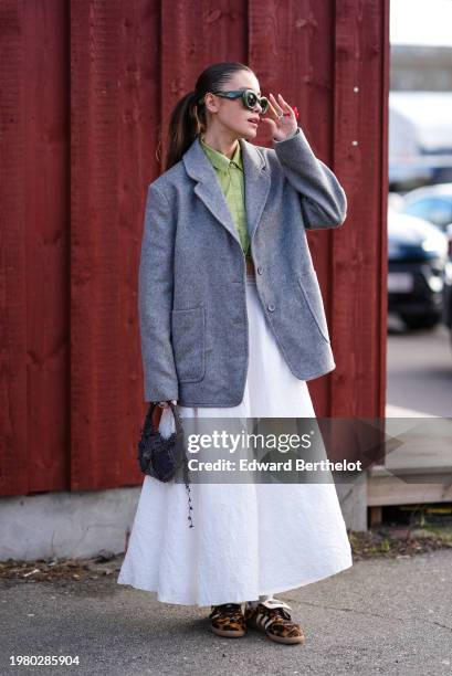 Guest wears green sunglasses from Loewe, a green shirt, a gray oversized blazer jacket , a white gathered midi dress, brown leopard print pattern...