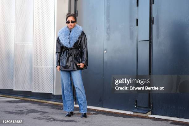 Ellie Delphine wears sunglasses, golden earrings, a black leather jacket with fluffy blue collar and lapels, blue denim jeans pants , black leather...