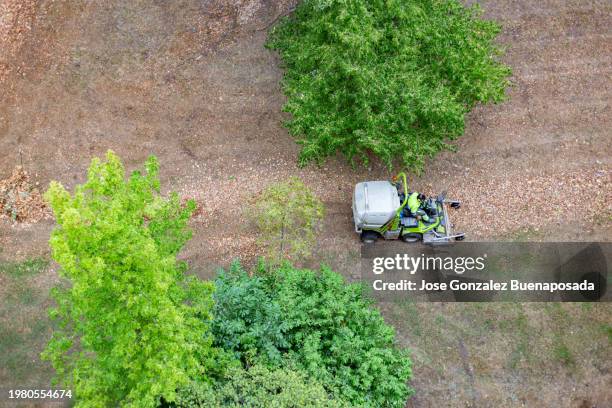 aerial view of a gardener driving a leaf vacuum machine in a public park garden. - leaf blower stock pictures, royalty-free photos & images