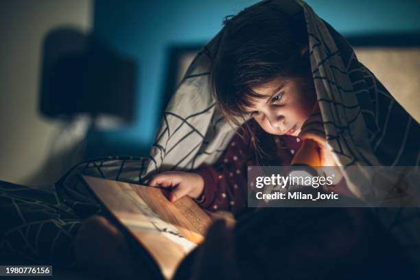 bambina che legge un libro sotto una coperta al buio - torcia elettrica foto e immagini stock