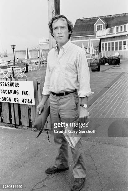 View of American television host Dick Cavett as he holds a hat and a copy of the New York Times, Montauk Point, Long Island, New York, August 4,...