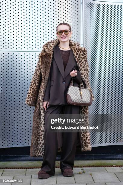 Guest wears sunglasses, golden earrings, a golden necklace, a brown leopard print pattern fluffy long coat, a brown oversized blazer jacket , a Gucci...