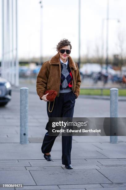 Renia Jaz wears aviator sunglasses, earrings, a brown aviator jacket with fluffy inner lining , an argyle pattern colored pullover , suit flared...