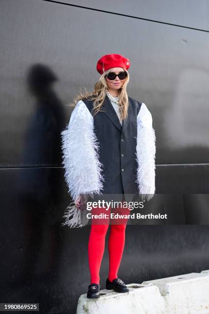 Guest wears a red beret hat with Chanel details, sunglasses , a pearl necklace, a gray oversized blazer jacket with white fluffy sleeves, red...