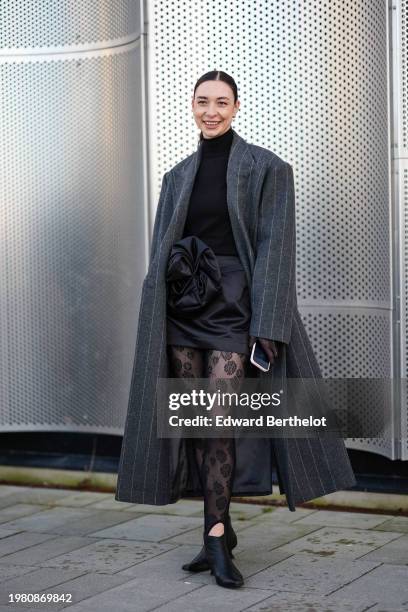 Guest wears a black turtleneck pullover , a gray oversized long striped coat , a black lustrous shiny silk mini skirt with floral detail, black...