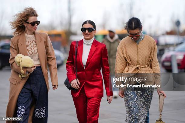 Guest wears a beige coat, a Loewe pullover, Loewe jeans ; a guest wears sunglasses, a turtleneck, a red lustrous shiny silk blazer jacket ; a guest...