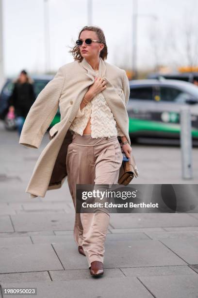 Guest wears sunglasses, a white fluffy long coat, a fluffy jacket with embroidered geometric patterns, beige palazzo flared pants , a brown leather...