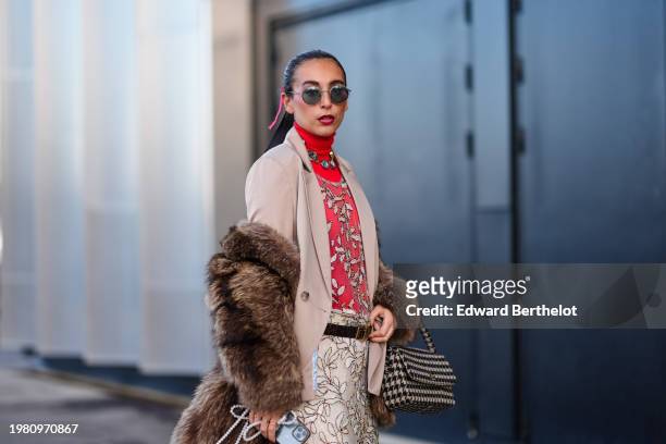 Gabriella Berdugo wears sunglasses, a bejeweled necklace , a red turtleneck pullover with white floral print , a brown fluffy faux fur coat, a beige...