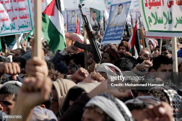 Houthi followers lift rifles, anti-U.S. And Israel emblems, placards depicting Houthi leader Abdul Malek Bard Alden Al-Houthi, and flags of Yemen and...