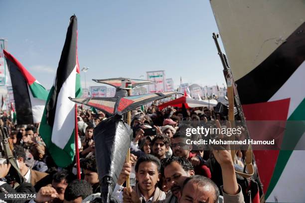 Houthi followers lift rifles, anti-U.S. And Israel emblems, placards depicting Houthi leader Abdul Malek Bard Alden Al-Houthi, and flags of Yemen and...