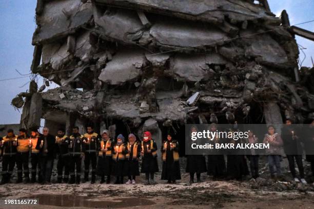 Members of the Syrian Civil Defence stand in a candle-lit remembrance vigil with survivors of the February 6, 2023 earthquake that devastated...