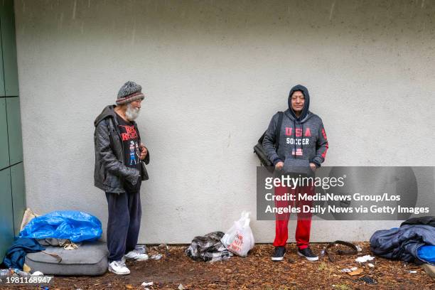 Los Angeles, CA Raul Moridal and Brigido Lopez, who are unhoused, keep out of the rain under a building awning at Tiara Street Park in North...