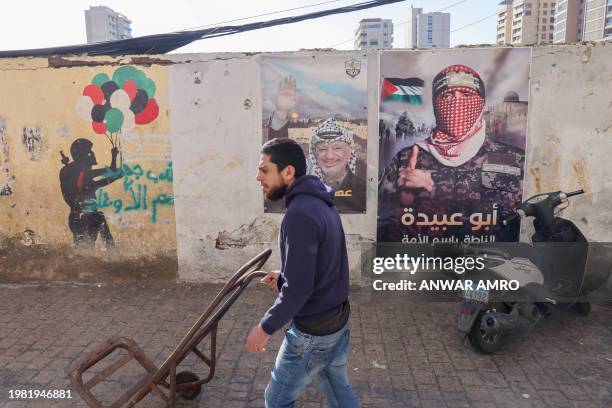 Man pushes a cart past posters depicting late Palestinian leader and president Yasser Arafat and spokesman for the militant group Hamas's armed wing...