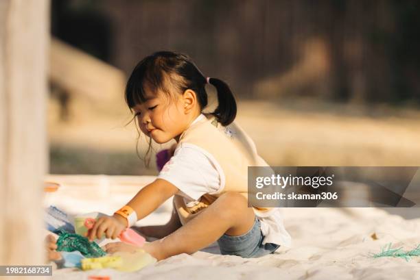 concentrated young child playing with colorful sand toys on a sandy beach during a sunny day. - sandkasten stock-fotos und bilder