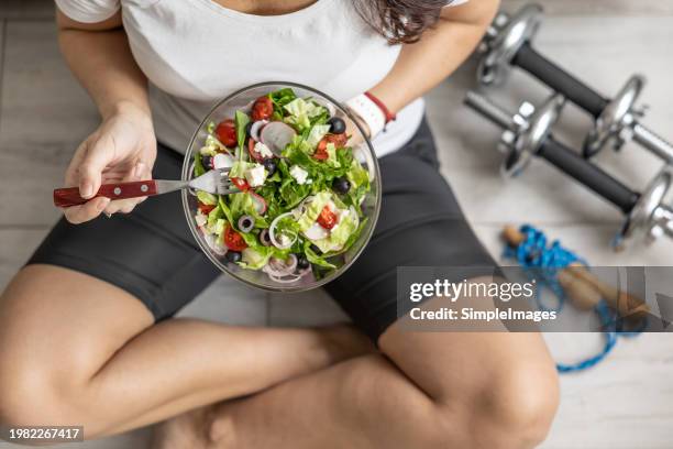 a fit woman in her forties eating a healthy salad after exercise. concept of healthy lifestyle. - afvallen stockfoto's en -beelden