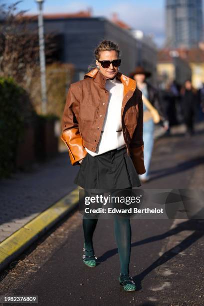 Guest wears sunglasses, a brown jacket with leather parts, a white top, a black mini pleated skirt , green tights, green checkered flat shoes,...