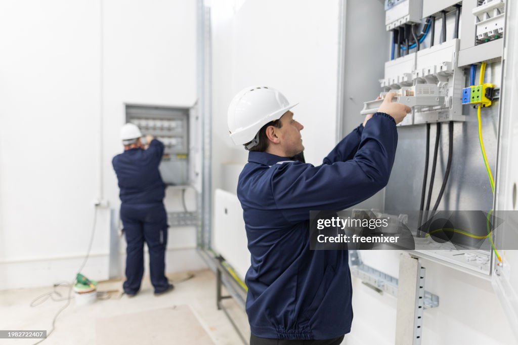 Two male electricians working in an electrical system control cabinet
