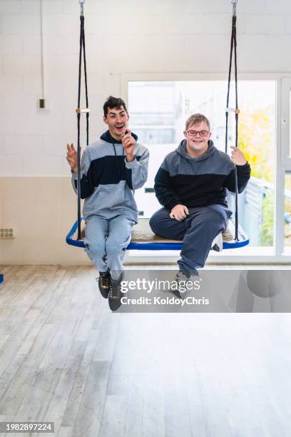 two joyful young friends with disabilities singing on a swing - promises rehab center foto e immagini stock