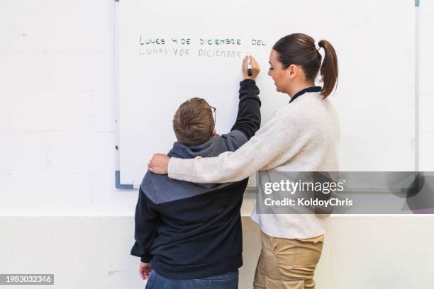 supportive educator assists student with down syndrome at board - promises rehab center foto e immagini stock