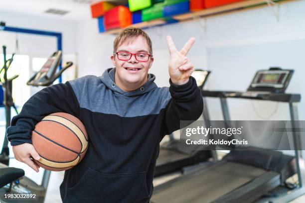 young man with down syndrome sharing victory sign in gym - basketball all access stock pictures, royalty-free photos & images