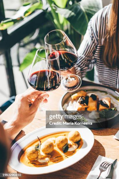 couple tasting red wine on a romantic date. a couple drinks red wine and clicks glasses. - vino tinto fotografías e imágenes de stock