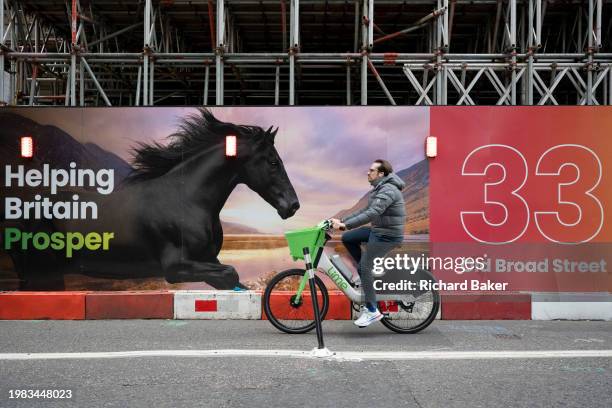 Cyclist passes an ad for the Lloyds Banking Group which features the finance brand's famous black stallion in the City of London, the capital's...