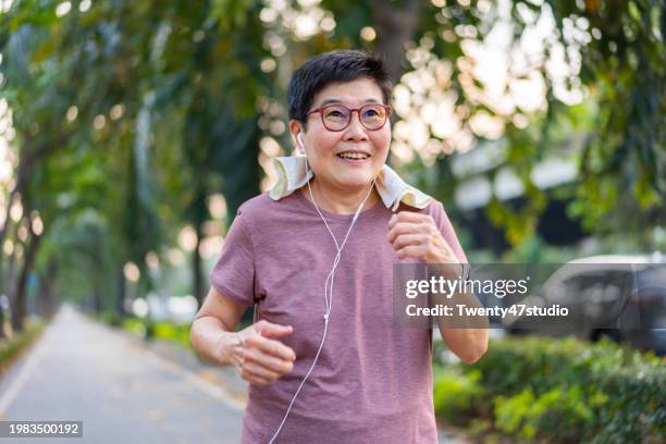 a senior woman wearing earphones while walking for exercise - technique de relaxation photos et images de collection