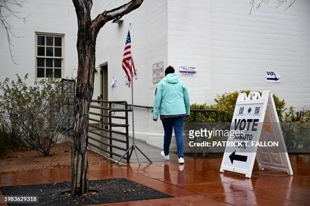 Person walks in the rain past signage displayed outside of a vote center on Election Day during the Nevada 2024 presidential primary election in Las...