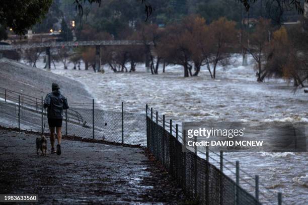Man jogs with a dog near the rain swollen Los Angeles River as a historic atmospheric river storm inundates Los Angeles, California, on February 6,...