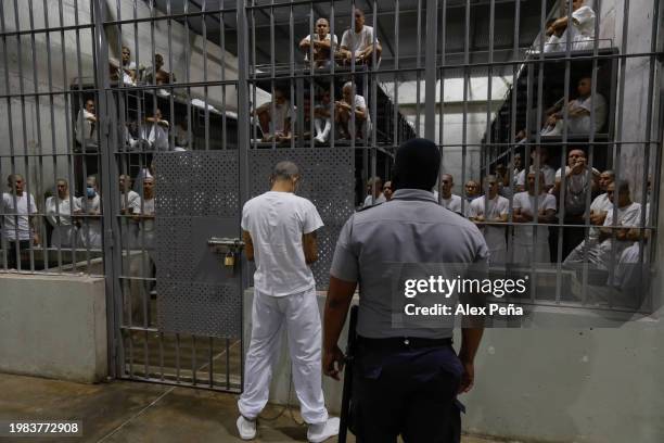 An inmate stands outside a cell as an officer stands on patrol at CECOT in Tecoluca on February 6, 2024 in San Vicente, El Salvador. On February of...