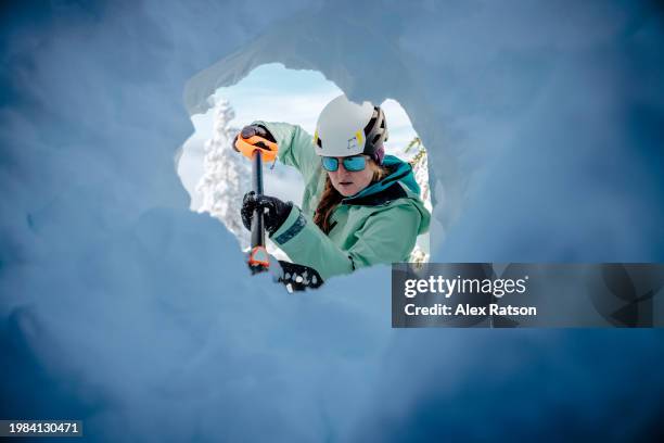 a woman digs a snow cave with a shovel in the alpine - lawine stockfoto's en -beelden