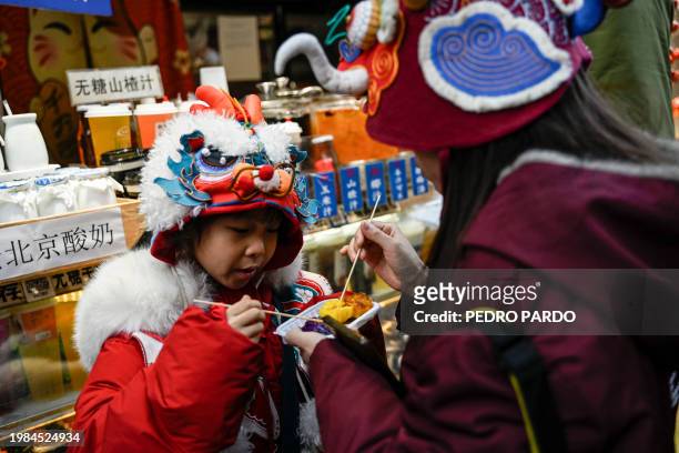 Toddler wearing a hat with a dragon figure eats snacks on a street at the Qianhai Lake tourist area in Beijing on February 7 ahead of the Lunar New...