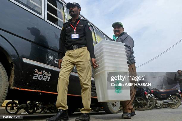 An election presiding officer is assisted by a policeman as they leave after collecting voting materials at a distribution center in Karachi on...