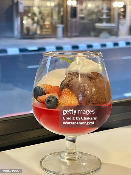 wine glass dessert - chocolate ice cream with slices of fruit on the red jelly base in a cup of wine glass.  street view background. - half street stock pictures, royalty-free photos & images