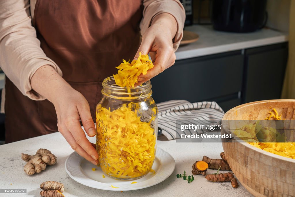 Woman putting sauerkraut in glass jar at kitchen counter