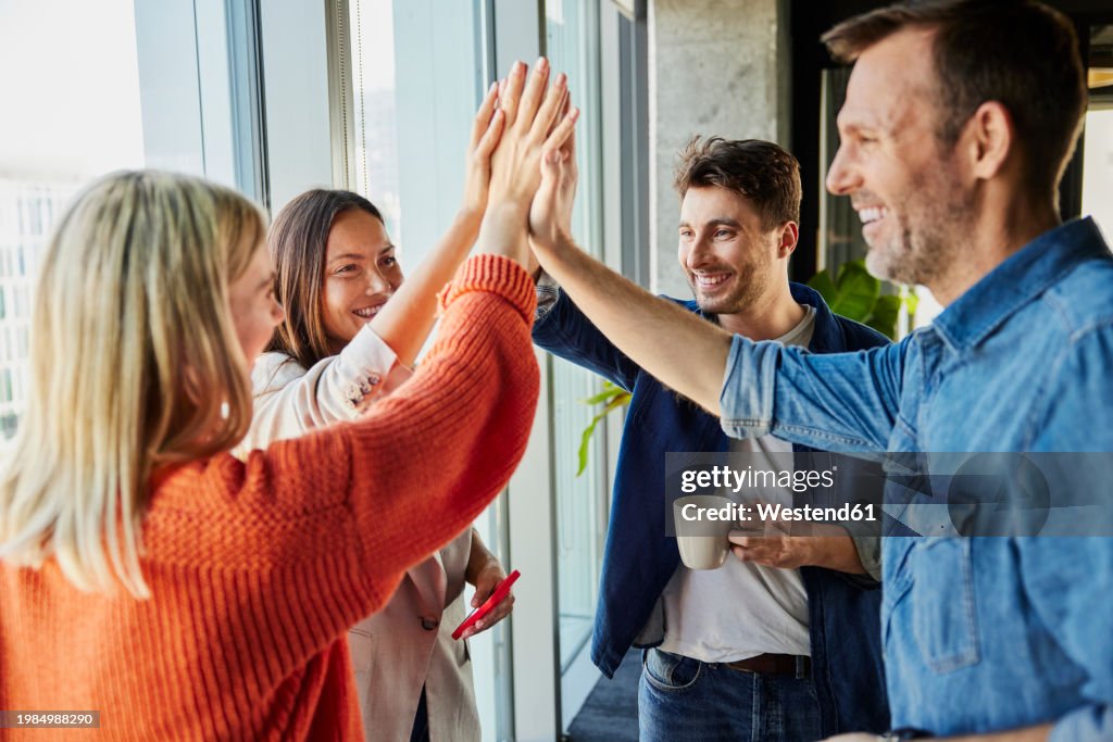 Happy businessmen and businesswomen giving high-five together in office