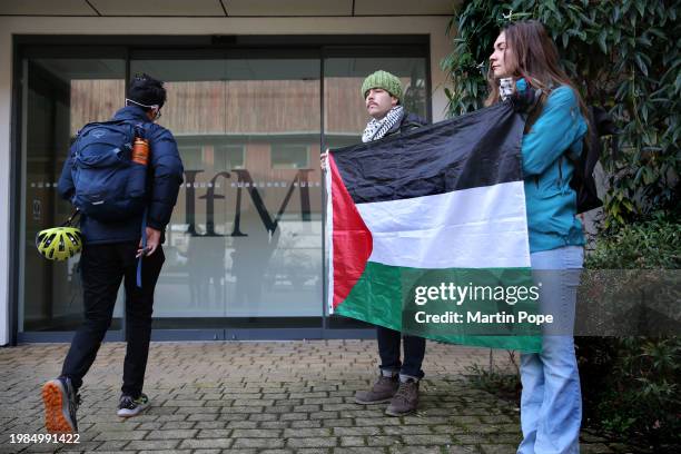 Protesters hold a Palestinian flag outside the Institute as a student arrives on February 7, 2024 in Cambridge, England. Supporters of "Demilitarise...