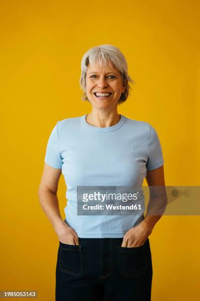 happy woman with hands in pockets against yellow background - hands in pockets stock pictures, royalty-free photos & images