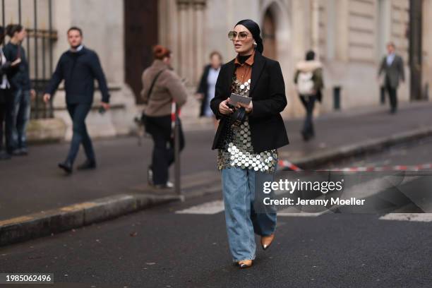 Fashion week guest is seen wearing a black turtleneck sweater over a brown satin blouse with large silver sequins, a black blazer, a black satin...