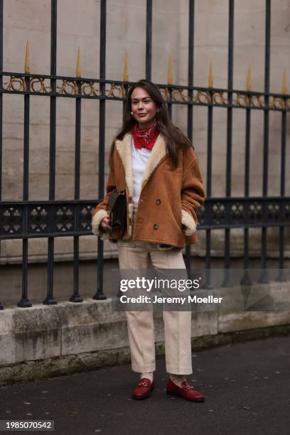 Fashion week guest is seen wearing a white top with a red and white scarf around the neck, an oversized brown jacket with fur details on the collar...
