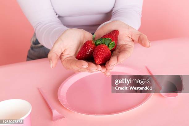 woman holding strawberries in hand over pink empty plate - hands cupped empty ストックフォトと画像